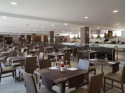 Ristorante d'hotel moderno e luminoso con tavoli e sedie marrone scuro apparecchiati per gli ospiti.
