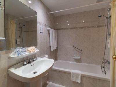 Prosta łazienka hotelowa z umywalką, wanną, ręcznikami i zasłoną prysznicową w neutralnych kolorach.