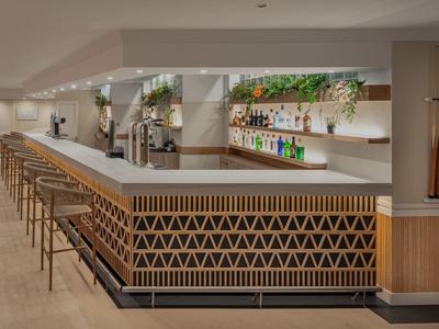 Area bar moderna in hotel con sgabelli di legno e banco decorativo sotto luce calda.