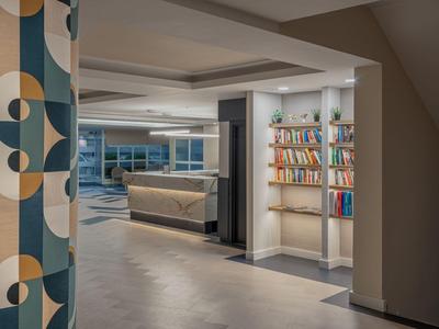 Reception di hotel moderna con banco elegante e scaffale per libri sotto illuminazione indiretta.