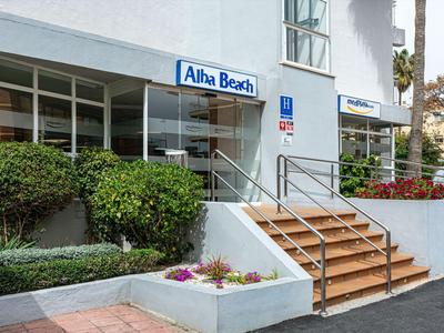 Ingresso di un hotel con scale in legno e cespugli verdi ai lati.