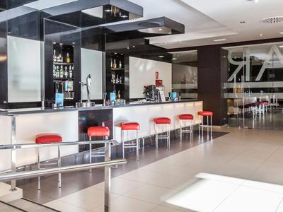 Moderner Hotelbarbereich mit weißem Tresen, roten Hockern und gut beleuchtetem Raum.