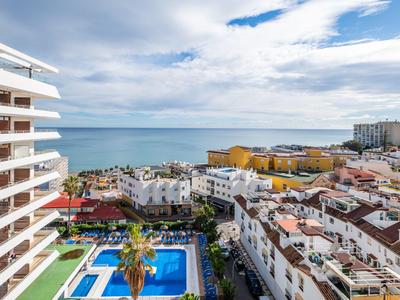 Blick auf eine Küstenstadt mit Hotels, Pool und Meer unter einem bewölkten Himmel.