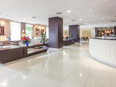 Geräumige Hotel-Lobby mit weißen Fliesen, Theke und Sitzbereich mit Sofas und Dekoration.