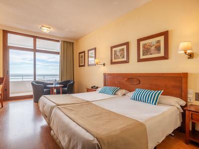 Hotelzimmer mit Doppelbett, Holzfußboden, Balkon mit Meerblick und neutralen Farben.