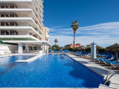 Moderner Hotelpool mit Liegestühlen und Sonnenschirmen unter klarem blauem Himmel.