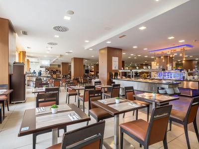 Modernes Restaurant mit vielen Tischen und Stühlen, hell beleuchtet und mit Buffetbereich.