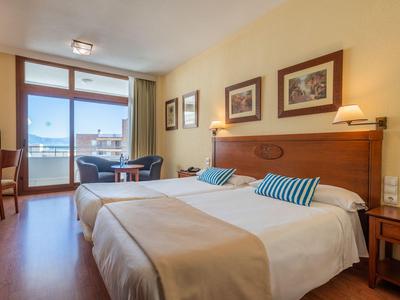 Hell eingerichtetes Hotelzimmer mit Doppelbett, Schreibtisch und Balkon mit Meerblick.
