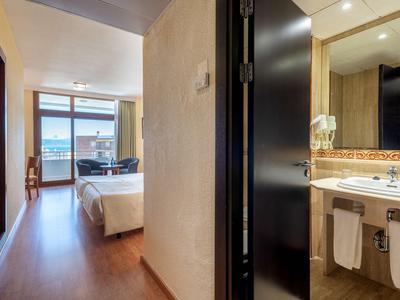 Modern eingerichtetes Hotelzimmer mit Bad, Holzboden und Blick auf den Balkon.
