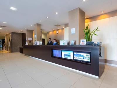 Nowoczesna recepcja hotelowa z podświetlanym recepcyjnym i personelem w tle.