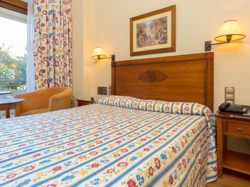 Gemütliches Schlafzimmer mit Doppelbett, gemustertem Bettbezug, Holzmöbeln und warmem Licht.