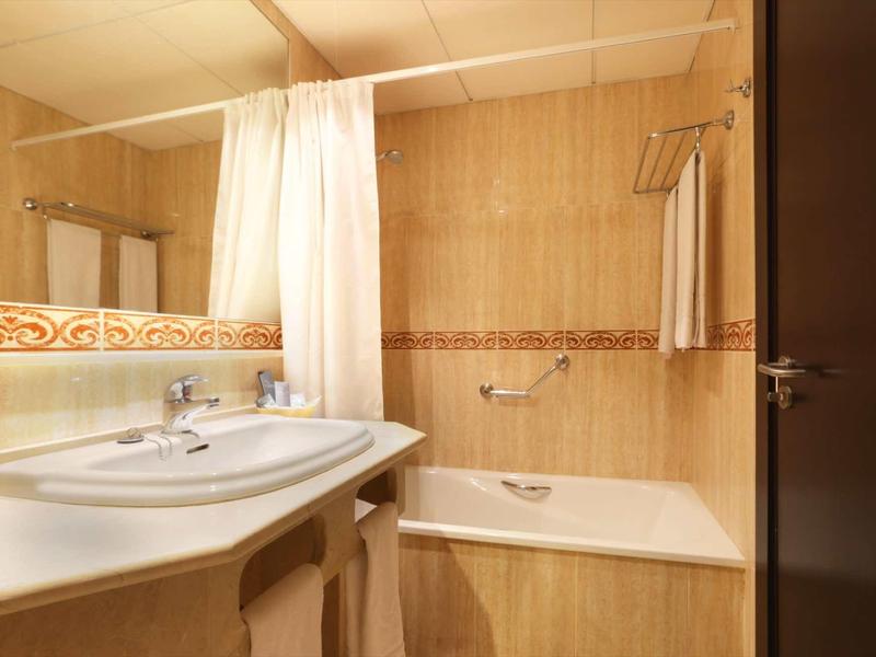 Helles Badezimmer mit beige gefliesten Wänden, weißem Waschbecken, Badewanne und Vorhang.