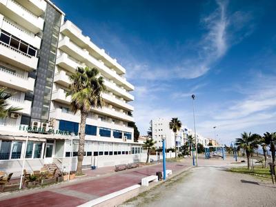 Complejo hotelero moderno con palmeras a lo largo de un amplio paseo marítimo bajo cielo azul.