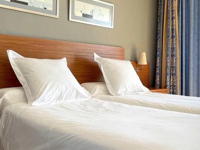 Jasny pokój hotelowy z dwoma pojedynczymi łóżkami, białymi poduszkami i pościelą przy oknie z zasłoną.