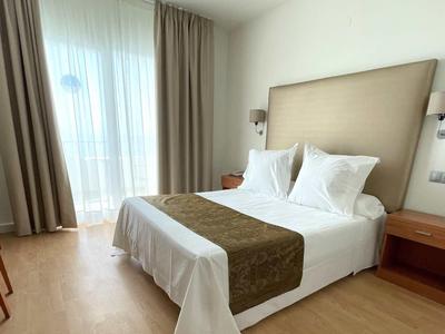 Nowoczesny pokój hotelowy z łóżkiem podwójnym, biurkiem, telewizorem i dużym oknem z zasłonami.