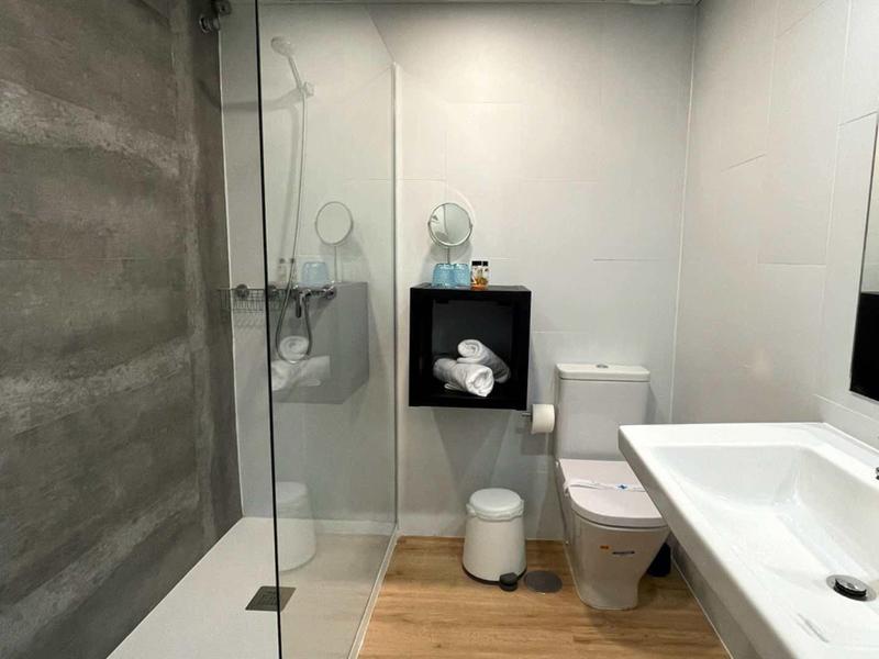 Moderner heller Badezimmer mit Glas-Duschabtrennung, weißer Toilette und Holzfußboden.