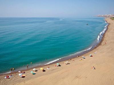 Breiter Sandstrand mit bunten Sonnenschirmen und ruhigem, blauem Meer unter klarem Himmel.