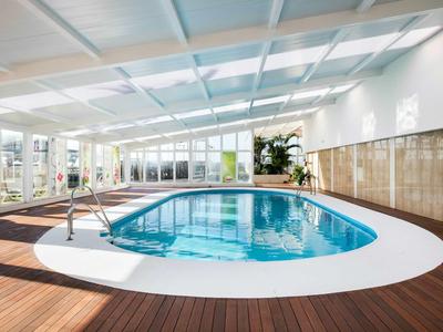 Hallenbad mit Holzfußboden, weißen Wänden und großen Fenstern für Tageslicht.