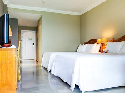 Hotelzimmer mit zwei großen Betten, Holzmöbeln und Fernseher auf einem Sideboard.