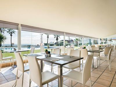 Moderner Speisesaal mit weißen Stühlen und Tischen mit Blick auf den Garten und das Meer.