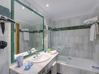 Helles Badezimmer mit Marmorfliesen, großer Spiegel und Badewanne.