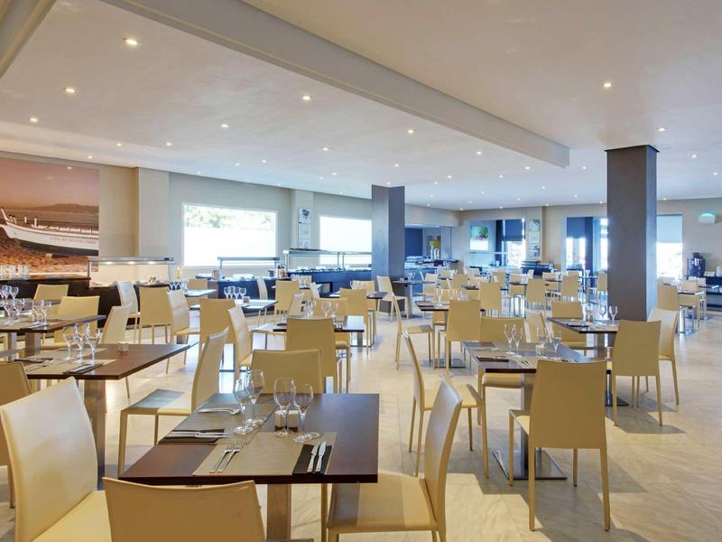 Ein großes, modernes Restaurant mit vielen hellen Stühlen und braunen Tischen, gut beleuchtet.