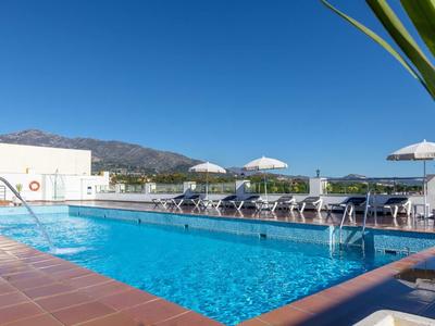Vista di una piscina all'aperto con lettini e ombrelloni bianchi, montagne sullo sfondo.