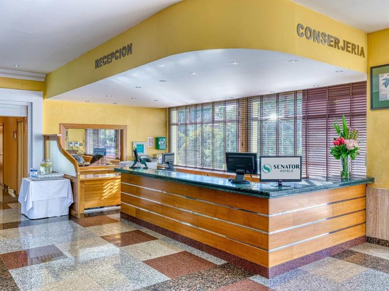 Helle Rezeption mit Holztheke, Marmorfußboden, gelben Wänden und großem Fenster im Hintergrund.