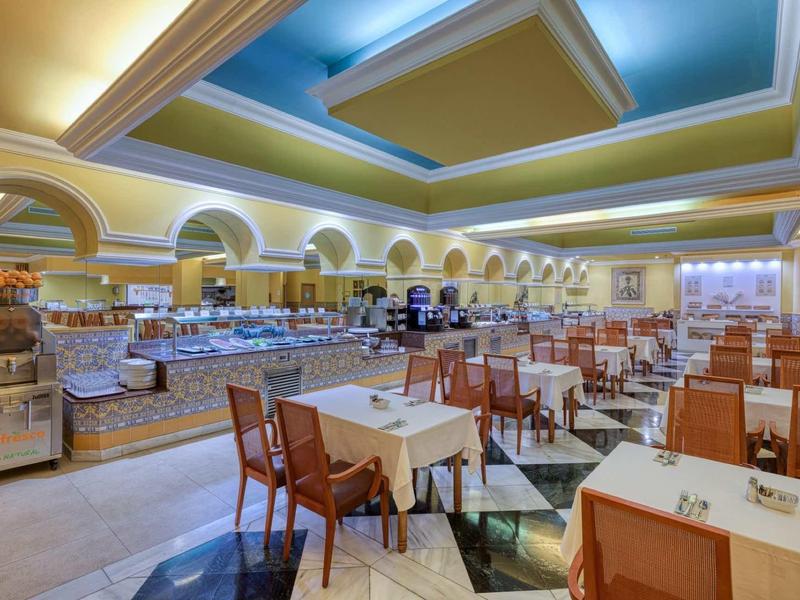 Großer Speisesaal mit zahlreichen Holztischen und Stühlen, heller Decke und Buffetbereich.