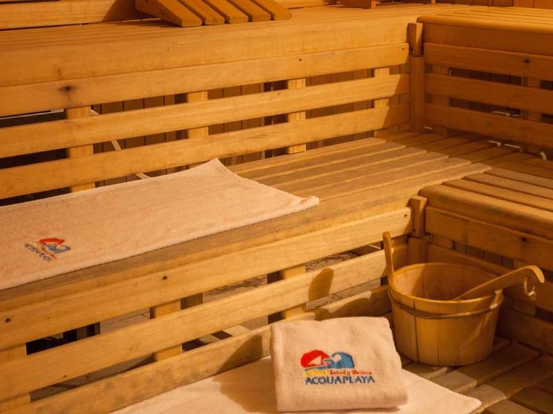 Holzsauna mit mehrstufigen Bänken, Holzeimer, -kelle und weißen Handtüchern.