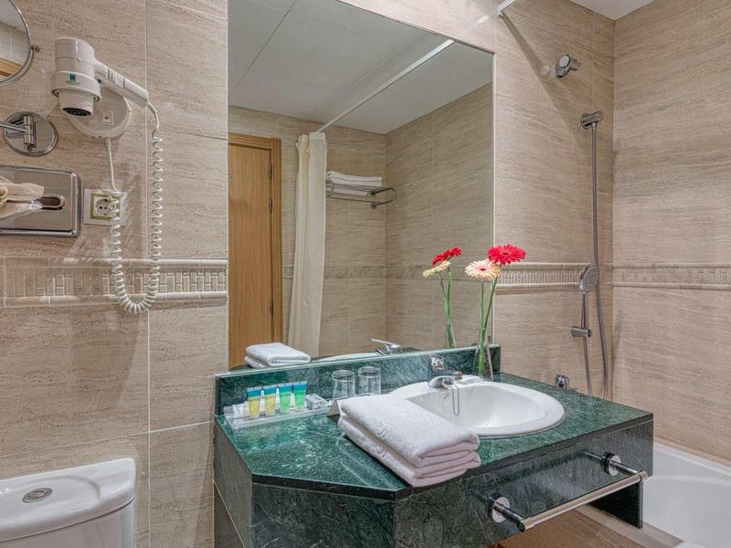 Modernes Badezimmer mit grünem Waschtisch, Spiegel, Badewanne und weißen Handtüchern.