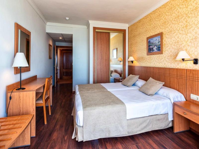 Modernes Hotelzimmer mit Doppelbett, Holzmöbeln und warmen Beige- und Brauntönen.