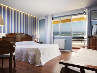 Habitación de hotel moderna con cama doble, zona de estar y vista al mar.