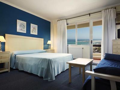 Habitación de hotel luminosa con cama doble, pared azul y balcón con vista al mar.