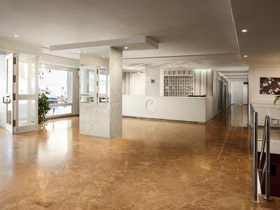 Luminoso vestíbulo de hotel con recepción, área de asientos y grandes ventanales con vista exterior.