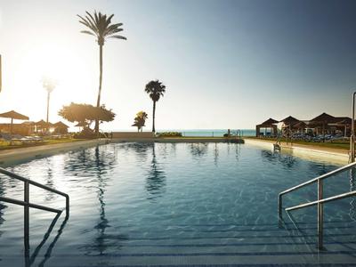 Vista de una piscina tranquila con palmeras y tumbonas al atardecer junto al mar