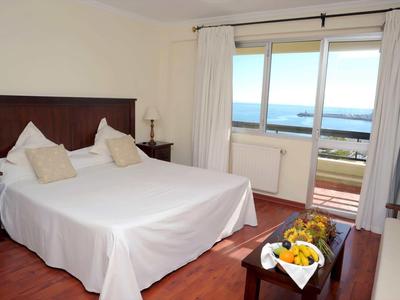 Dormitorio luminoso con cama doble, suelo de madera y vista al mar desde el balcón.