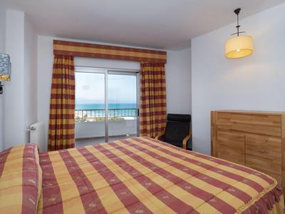 Schlafzimmer mit Doppelbett, Holzmöbeln und Blick auf das Meer durch eine Glasschiebetür.
