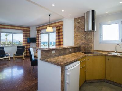 Moderne Wohnküche mit gelben Schränken, Steinwandakzent und Blick ins helle Wohnzimmer.