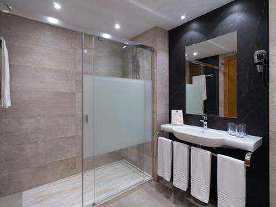 Moderne Hoteldusche mit Glaswänden, großen Spiegel und Waschbecken mit weißen Handtüchern.