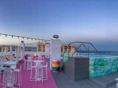 Dakterras met bar, ligstoelen en zwembad met uitzicht op zee bij zonsondergang.