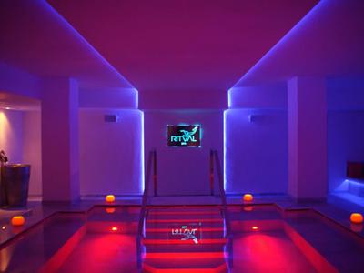 Moderner Wellnessbereich mit beleuchtetem Pool, violett-blauer Raumbeleuchtung und digitaler Anzeige.