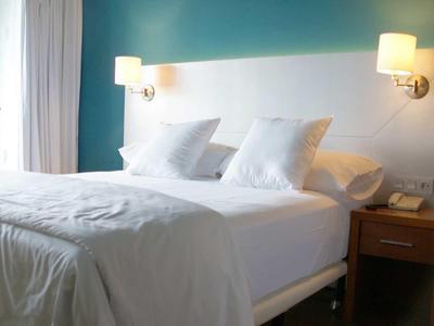 Modernes Schlafzimmer mit großem weißen Bett, zwei Nachttischen und hellblauem Wandhintergrund.