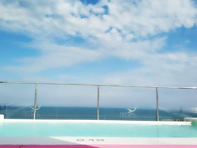 Ein klarer Pool mit Glasgeländer vor blauem Himmel und weitem Meer im Hintergrund.