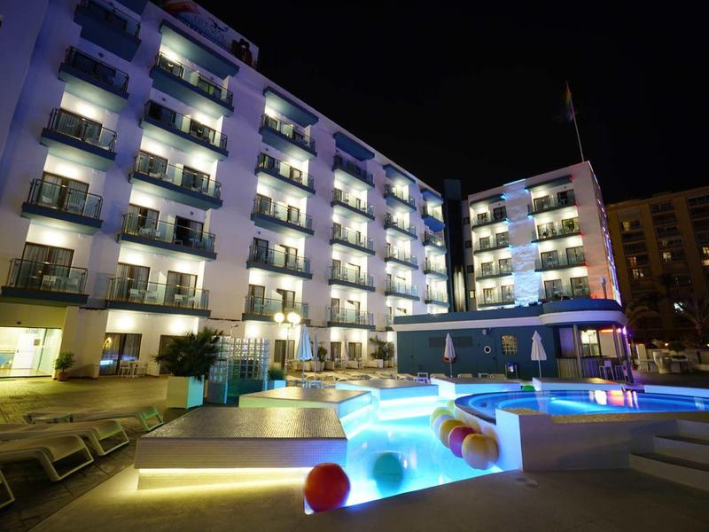 Beleuchtetes Hotel mit mehreren Balkonen und beleuchtetem Poolbereich in der Nacht.