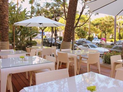 Area pranzo esterna vuota di un hotel con tavoli bianchi e ombrelloni sotto le palme.