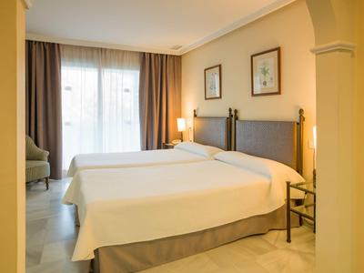 Stanza d'hotel luminosa con due letti singoli e una finestra con tende.