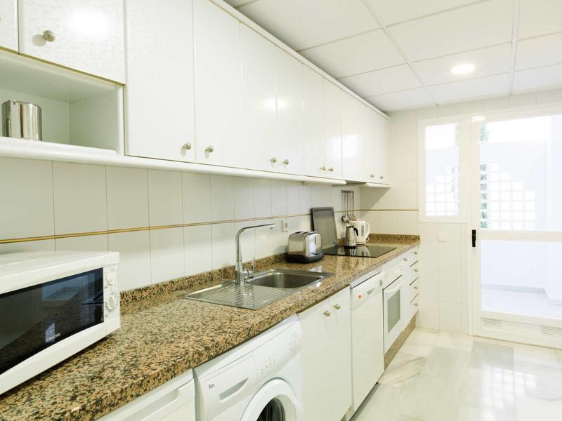 Moderne helle Küche mit weißem Schrank, Granit-Arbeitsplatte, Waschmaschine, Mikrowelle und Spüle.