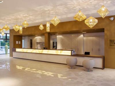 Moderner Hotellobby-Empfang mit langem weißen Tresen und hängenden goldenen Lampen.