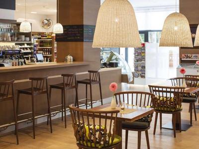 Modernes Café mit Holztischen, Stühlen und einer langen Theke mit Barhockern.